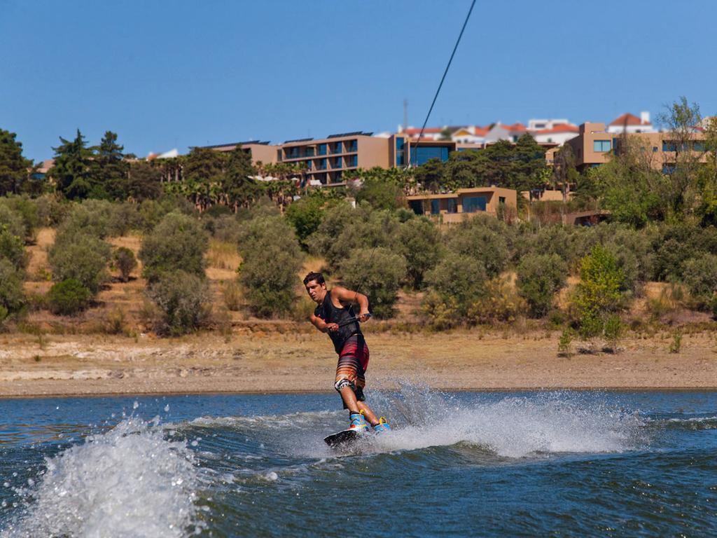 Ap Lago Montargil - Conference & Spa Zewnętrze zdjęcie The photo shows a person wakeboarding on a body of water. The individual is being pulled by a cable, which is likely connected to a boat or a winch. The person is wearing a life jacket and swim shorts, balancing on the board as they enjoy the activit