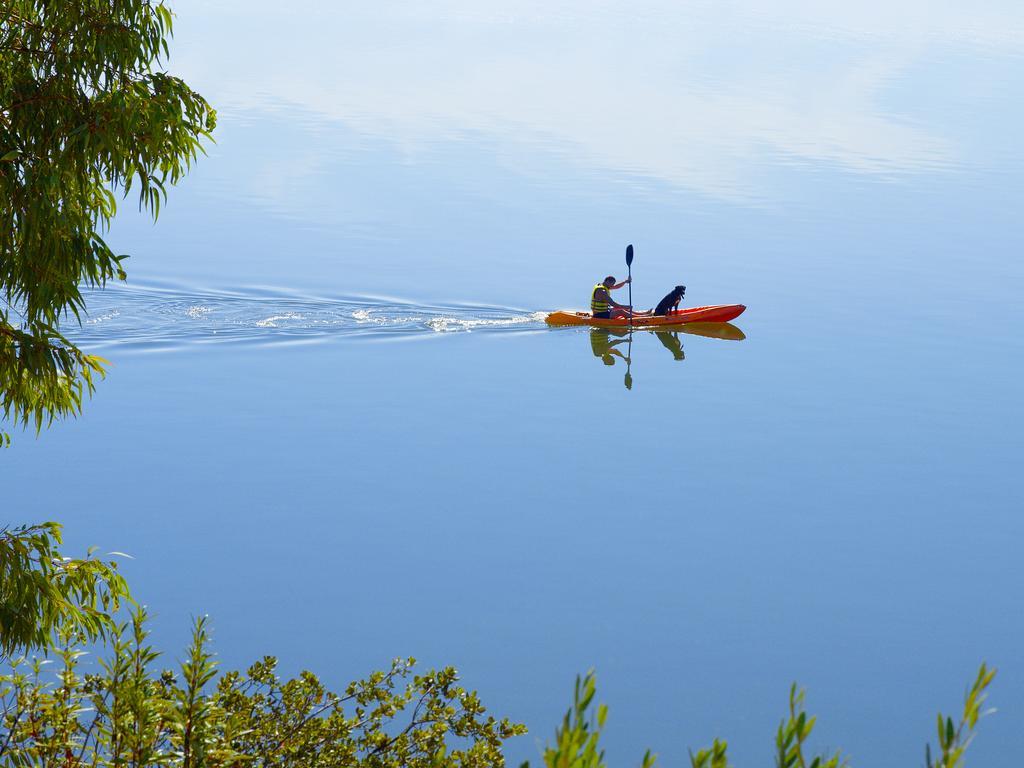 Ap Lago Montargil - Conference & Spa Zewnętrze zdjęcie The photo shows a serene scene of a person kayaking on a calm body of water. The surface of the water is very smooth, reflecting the surroundings, and there is a gentle wake behind the kayak indicating movement. The kayaker is wearing a life jacket a