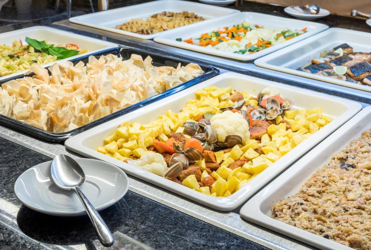 Ap Lago Montargil - Conference & Spa Zewnętrze zdjęcie The photo shows a buffet-style display of various dishes. There are several rectangular trays filled with different types of food. 

1. One tray contains a mix of vegetables and seafood, likely including potatoes and cauliflower.
2. Another tray hold