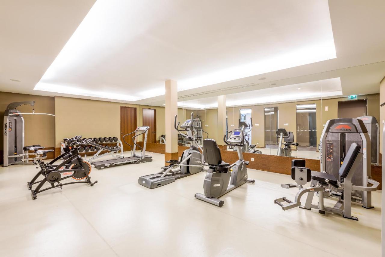 Ap Lago Montargil - Conference & Spa Zewnętrze zdjęcie The image shows a modern gym interior featuring various exercise equipment. On the left, there are free weights and weight benches. In the center, there are multiple machines, including a stationary bike and an elliptical. The space is well-lit with 