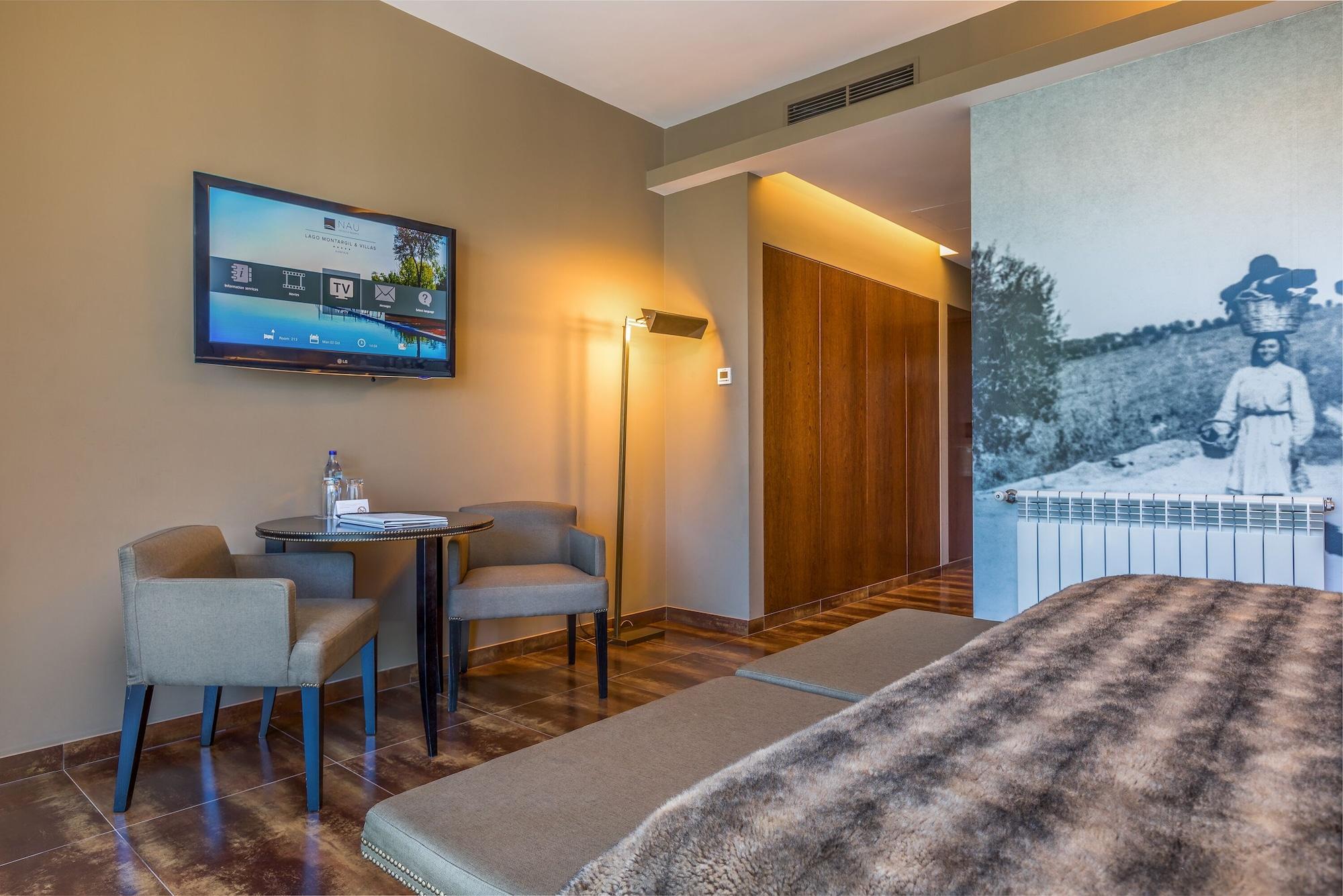 Ap Lago Montargil - Conference & Spa Zewnętrze zdjęcie The photo shows an interior of a room, likely a hotel or a modern living space. In the foreground, there is a bed with a textured brown blanket. To one side, there are two comfortable chairs and a small table, possibly with a bottle of water. A flat-