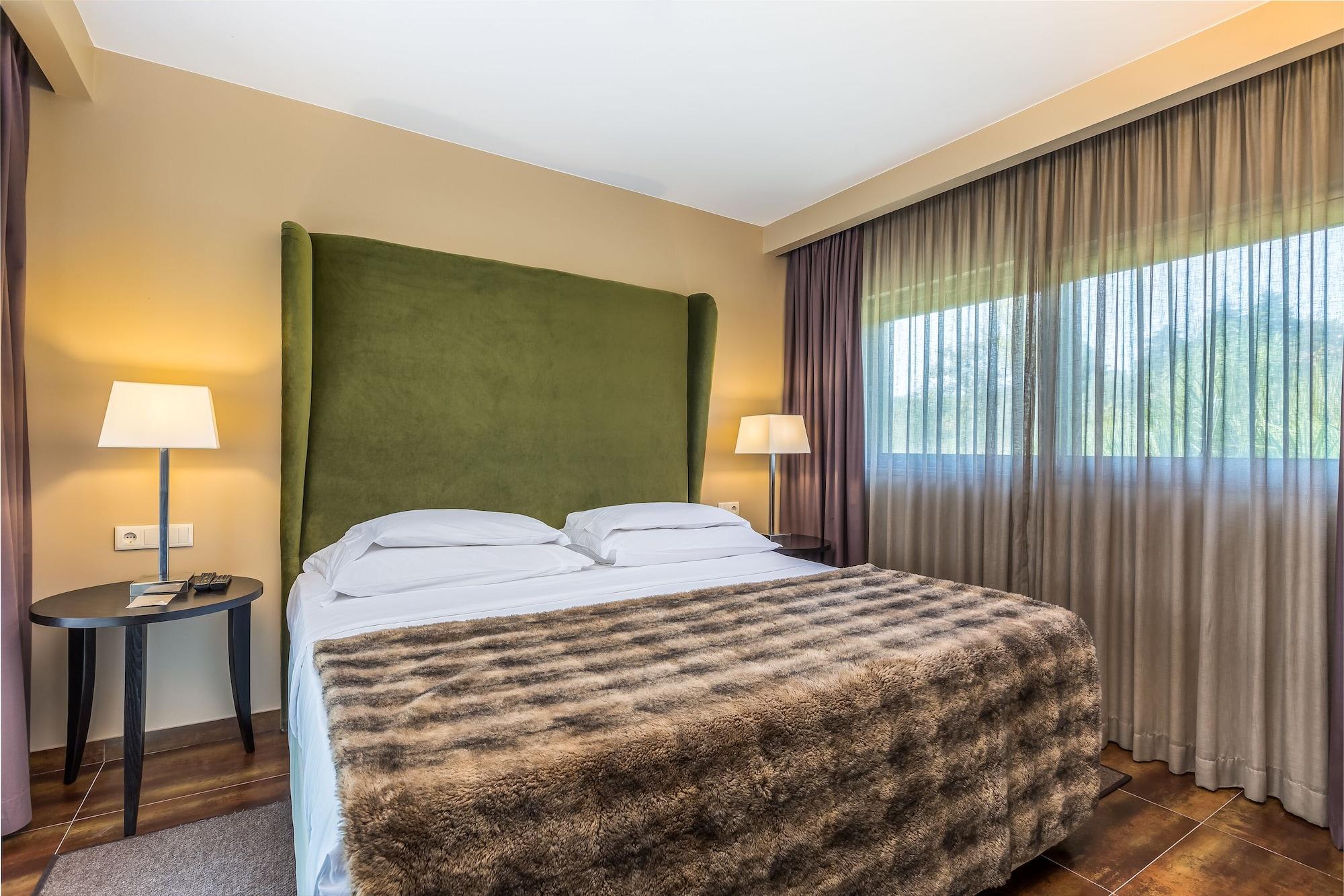 Ap Lago Montargil - Conference & Spa Zewnętrze zdjęcie The photo shows a cozy hotel room featuring a large bed with two white pillows and a fur-style blanket draped over it. Behind the bed is a tall, green headboard that adds a touch of color to the room. On either side of the bed are bedside tables, eac