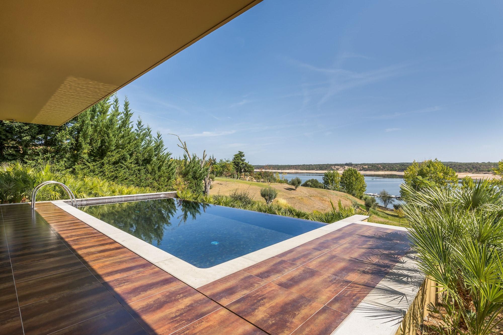 Ap Lago Montargil - Conference & Spa Zewnętrze zdjęcie The photo shows a luxurious infinity pool situated on a terrace or deck. The pool features a sleek, modern design with a dark blue surface that reflects the surrounding scenery. In the background, there is a landscape of rolling hills and a body of w