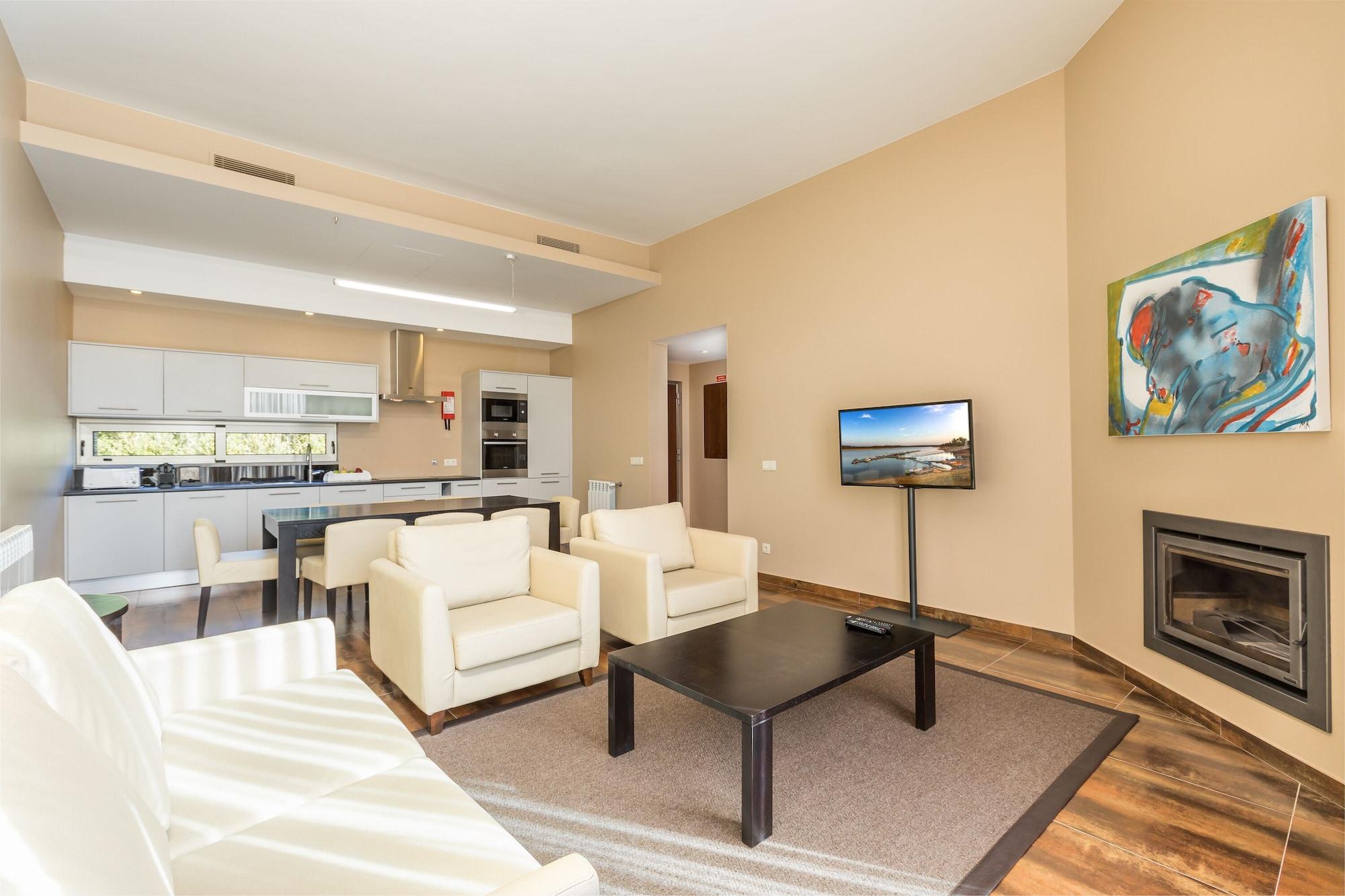 Ap Lago Montargil - Conference & Spa Zewnętrze zdjęcie The photo shows a modern, spacious living area with a contemporary design. The room features light-colored walls and wooden flooring. 

In the center, there is a black coffee table surrounded by four white armchairs. A flat-screen TV is mounted on th