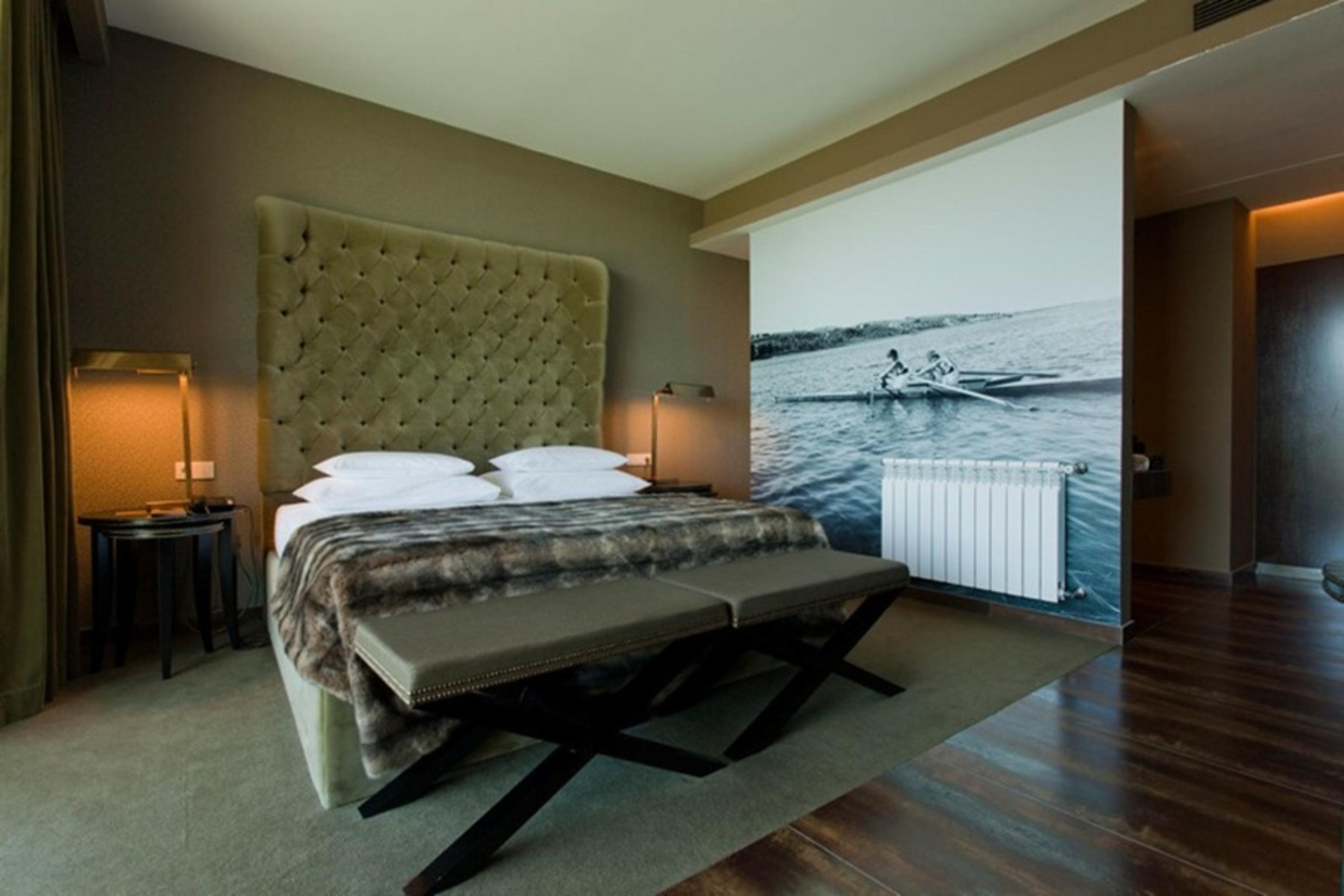 Ap Lago Montargil - Conference & Spa Zewnętrze zdjęcie The photo shows a modern hotel room featuring a large bed with a tufted headboard and plush bedding. The color palette is neutral, with shades of green and gray. On one side of the room, there are bedside tables with lamps. A comfortable bench sits a