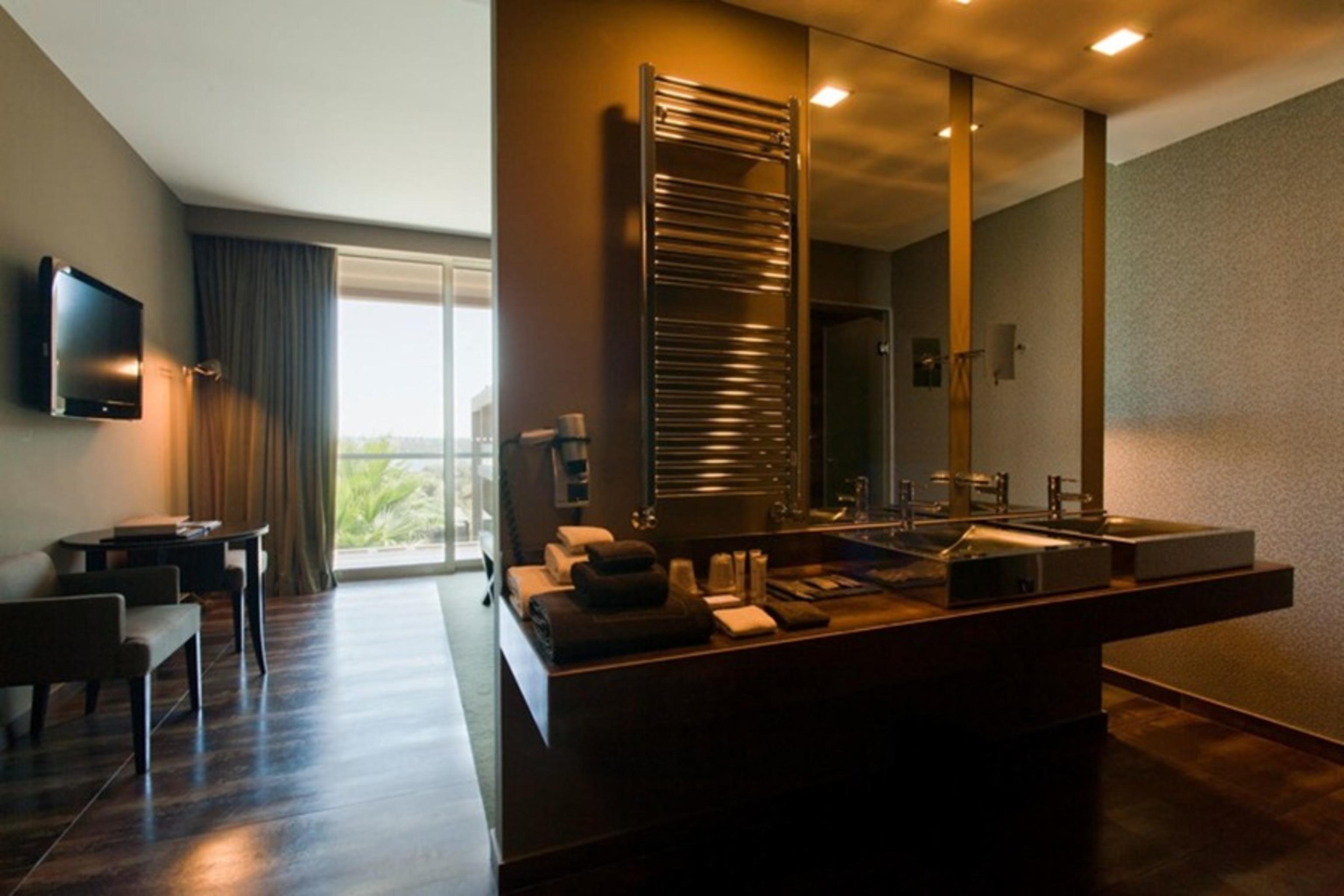 Ap Lago Montargil - Conference & Spa Zewnętrze zdjęcie The photo displays a modern hotel room with a contemporary design. The room features a large window, allowing natural light to enter and offering a view outside. On one side, there is a sitting area with a small table and chairs. The other side showc