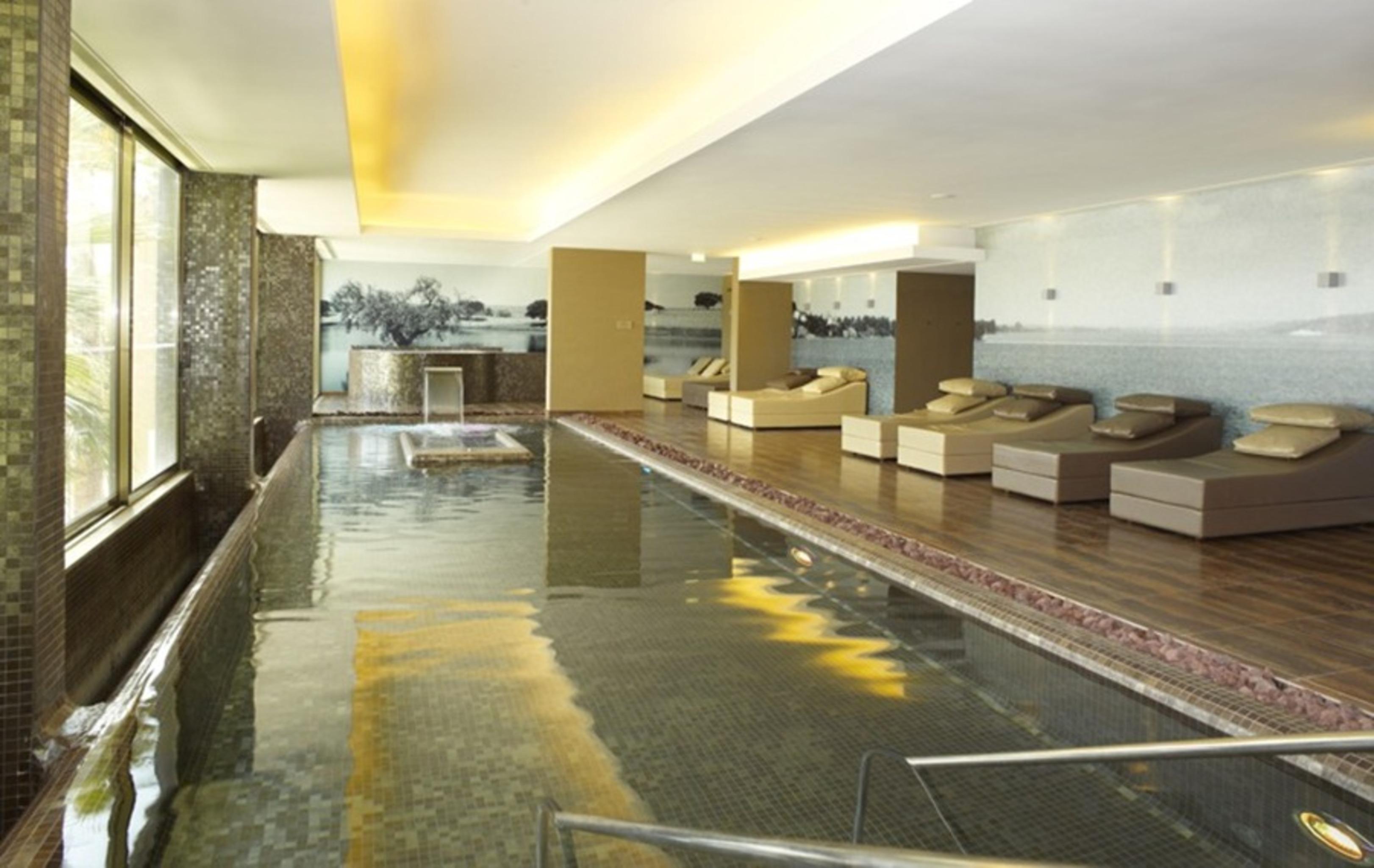 Ap Lago Montargil - Conference & Spa Zewnętrze zdjęcie The photo shows a modern, serene spa environment. There is a swimming pool with calm water, reflecting the surrounding decor. Along the sides, there are several comfortable lounge chairs arranged, perfect for relaxation. Large windows allow natural l
