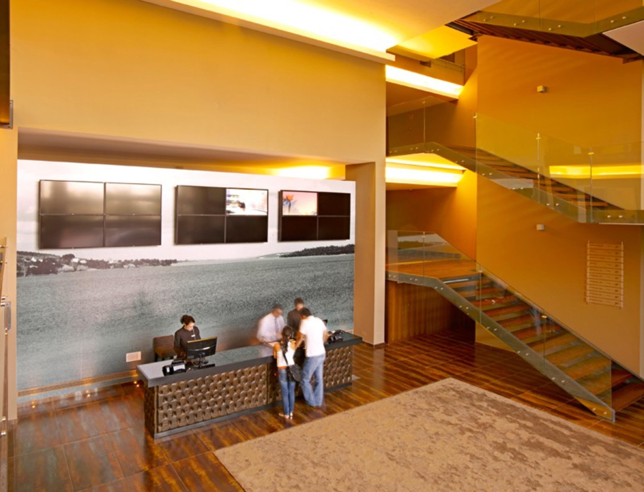 Ap Lago Montargil - Conference & Spa Zewnętrze zdjęcie The photo depicts a modern lobby area with a reception desk. The design features a combination of warm colors and wood flooring. In the background, there is a large wall-mounted screen or display, showcasing several monitors. The wall behind the desk