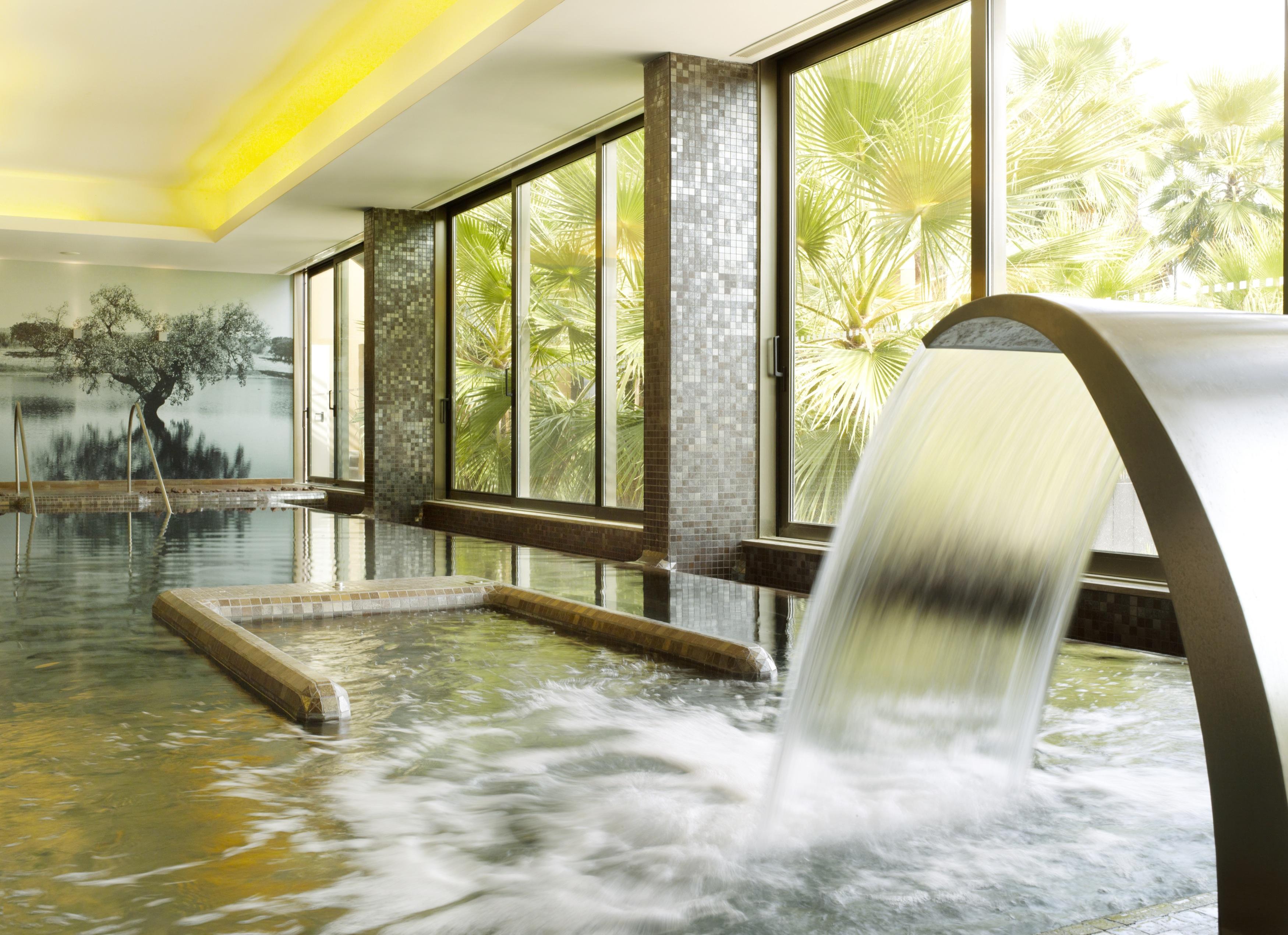 Ap Lago Montargil - Conference & Spa Zewnętrze zdjęcie The photo depicts a serene spa environment featuring a tranquil indoor pool area. There is a sleek, modern water feature that spills water gracefully into the pool. Large windows allow natural light to flood the space, showcasing views of lush greene