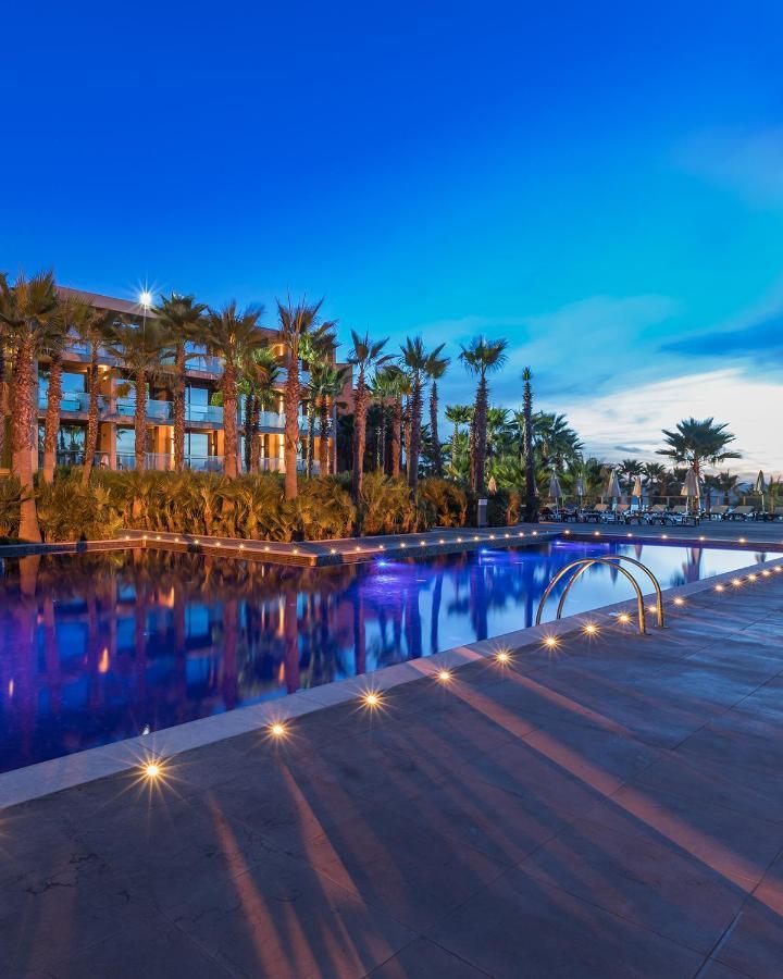 Ap Lago Montargil - Conference & Spa Zewnętrze zdjęcie The image shows a serene and inviting outdoor area with a large swimming pool that features a beautiful blue hue, likely illuminated by lights. Surrounding the pool are well-maintained palm trees and lush greenery, creating a tropical atmosphere. In 